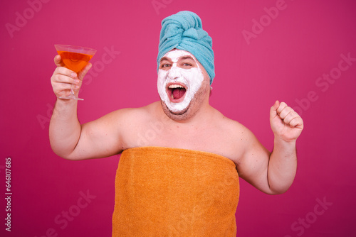Early morning. Funny fat man is preparing for a party and drinking a cocktail. Pink background.