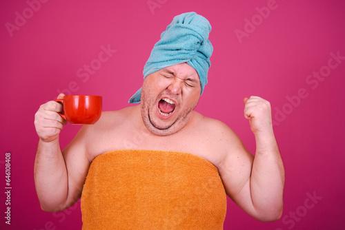 Early morning. Funny fat man gets ready for a party after a shower and eats donuts. Pink background.