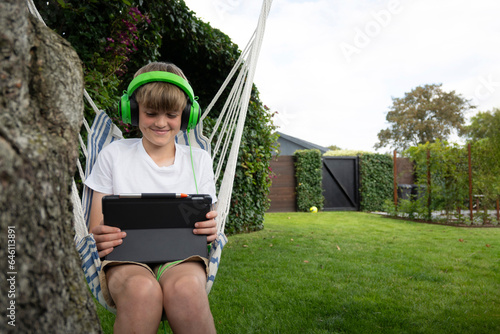 boy sitting in a hammock in the garden watching a video on his tablet with headphones  photo