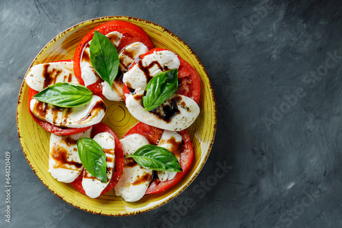 Salad Caprese with tomato, mozzarella and fresh basil on dark background. Top view. Copy space