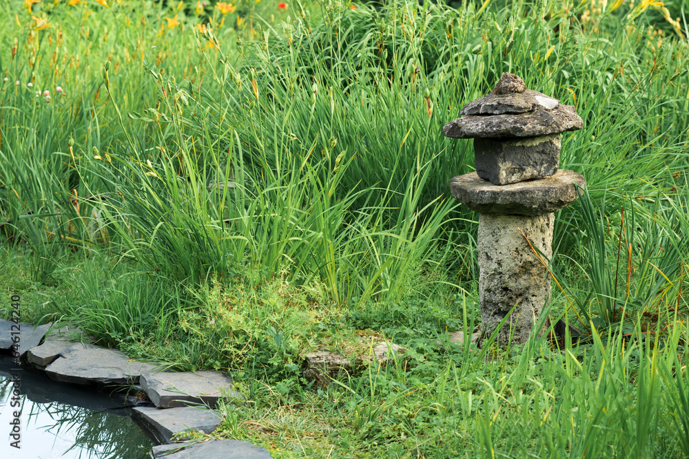 old stone lantern among grass on the bank of a pond in a Japanese garden old stone lantern among grass on the bank of a pond in a Japanese garden