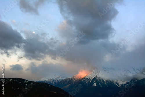 Big winter snowy mountains over which clouds fly by and the evening sun shines. Winter landscape