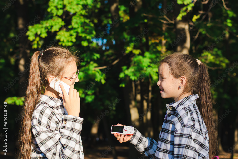 One girl gives another dump phone in a summer sunny park One girl gives another dump phone in a summer sunny park