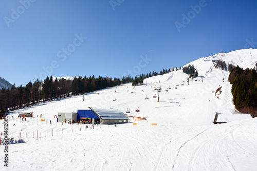 Mountain slope for downhill skiing with lift in perspective. Bright white snow and blue sky