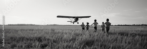 Black and white photograph, children running through a field of tall grass, a vintage biplane flying overhead, freedom and simplicity