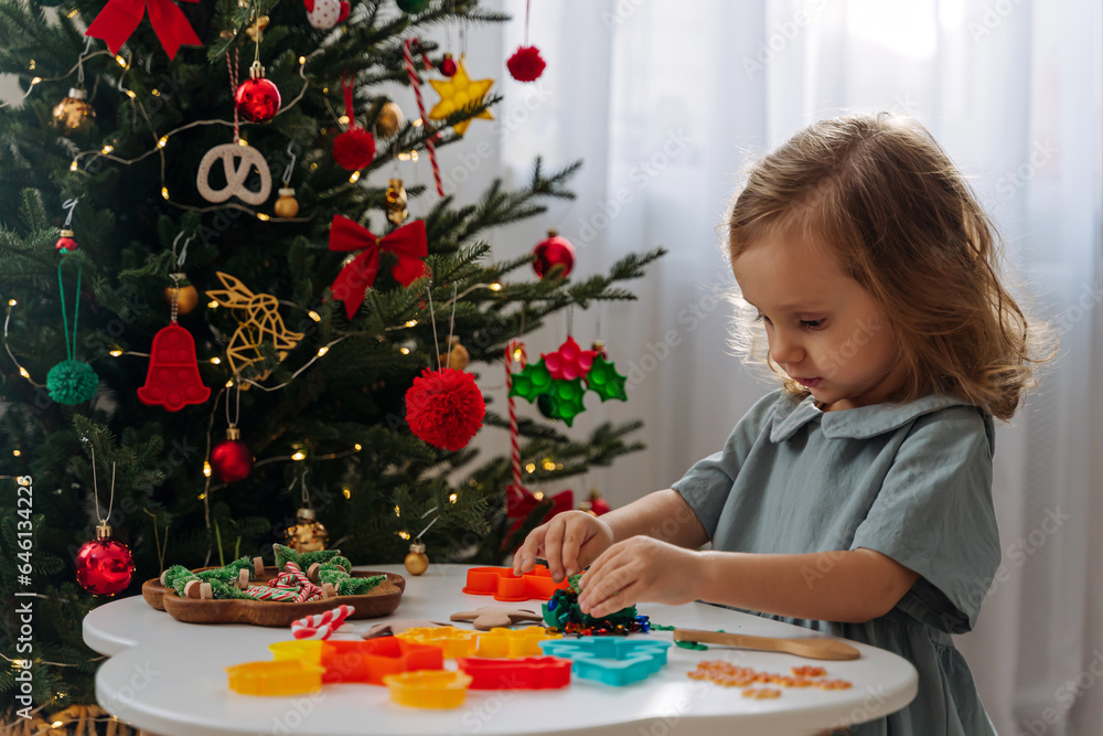 A little girl playing with play dough, plasticine and Christmas decorations. Child hands creating Christmas crafts. Holiday Art Activity for Kids. Sensory play for toddlers.. A little girl playing with play dough, plasticine and Christmas decorations. Child hands creating Christmas crafts. Holiday Art Activity for Kids. Sensory play for toddlers..