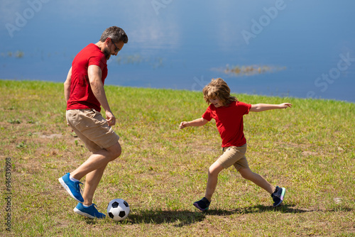 Dad with his little cute son are having fun and playing football on green grassy summer lawn. Football soccer sport concept. Father and son playing football. Father and kid play with soccer ball.