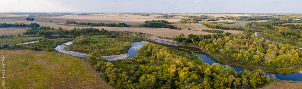 Aerial panorama of a winding river cutting through autumn-colored trees and scattered farmland.  The sky is a flat gray color.
