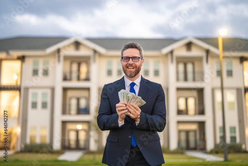 Portrait business man holding cash dollar bills front of house outdoor. Big luck. Dollar cash money concept. Rejoices to win cash. Man hold cash money. Financial luck and success. Manager or realtor. © Volodymyr