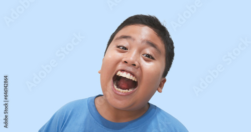 close-up portrait, a joyful and cheerful young boy is seen with a happy expression, mouth wide open, set against an isolated light blue background