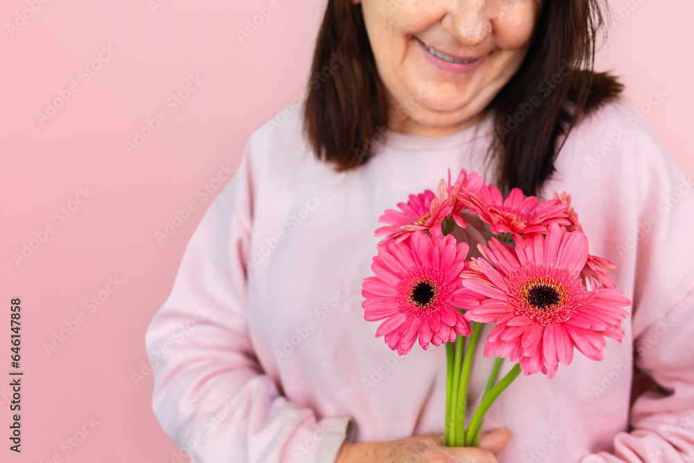 Mature Brazilian woman smiling while holding a bouquet of pink gerbera daisies, isolated against a pink background. Mature Brazilian woman smiling while holding a bouquet of pink gerbera daisies, isolated against a pink background.