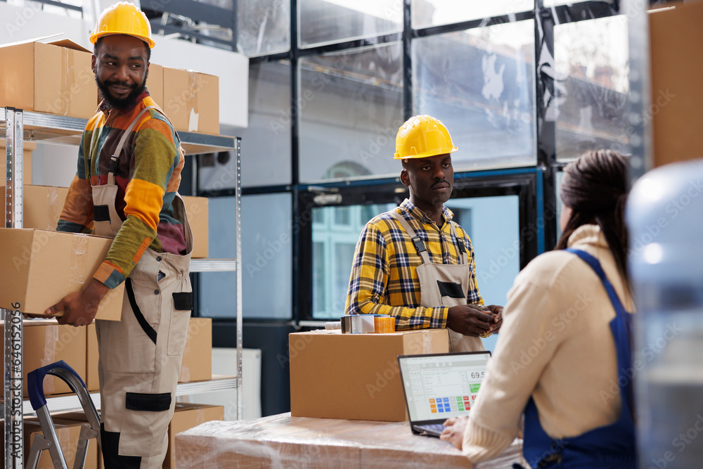 Warehouse package handlers and order picker working in storage room. Storehouse workers wearing safety hard hats taking cardboard boxes from shelf while manager checking products list Warehouse package handlers and order picker working in storage room. Storehouse workers wearing safety hard hats taking cardboard boxes from shelf while manager checking products list