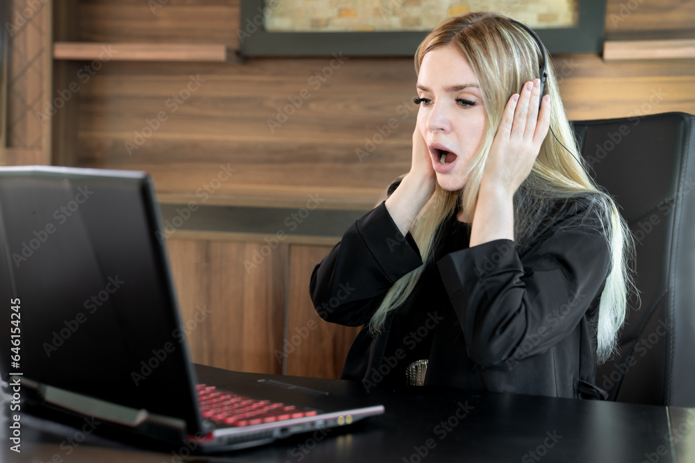 Young business woman sitting in front of laptop with expression of shock on her face with her mouth open and holding face with hands Young business woman sitting in front of laptop with expression of shock on her face with her mouth open and holding face with hands