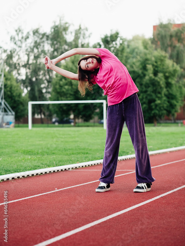 Young teenager girl doing stretching exercises on a running track. Selective focus. The model is slim body type. Light and airy look. Get ready for sport concept. Outdoor activity and lifestyle. © mark_gusev