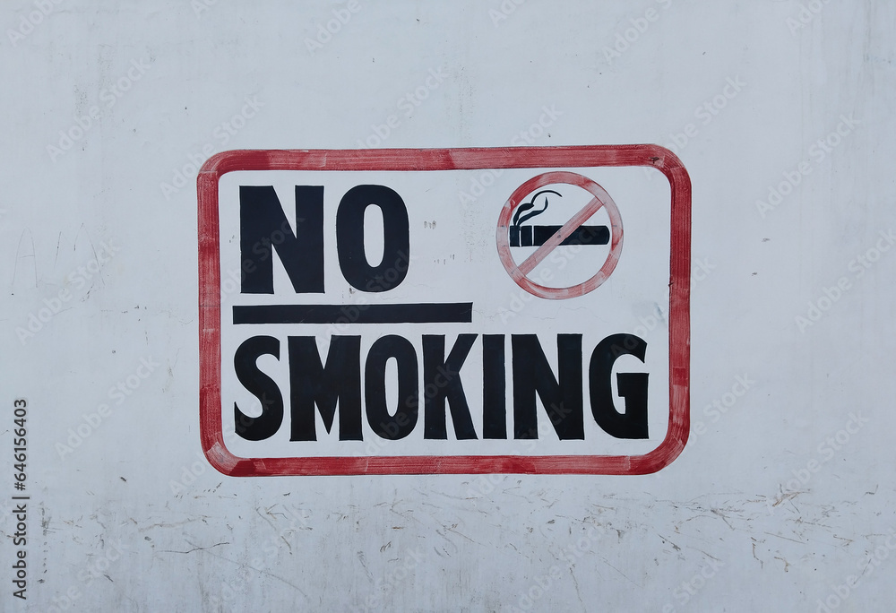 No smoking sign with a crossed out cigarette in a red square painted on a white wall No smoking sign with a crossed out cigarette in a red square painted on a white wall