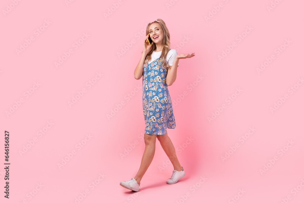 Full length profile portrait of lovely positive person speak chatting telephone walking isolated on pink color background Full length profile portrait of lovely positive person speak chatting telephone walking isolated on pink color background
