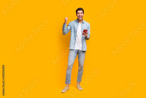 Photo of positive guy using device browsing web raise fist up winning isolated bright color background