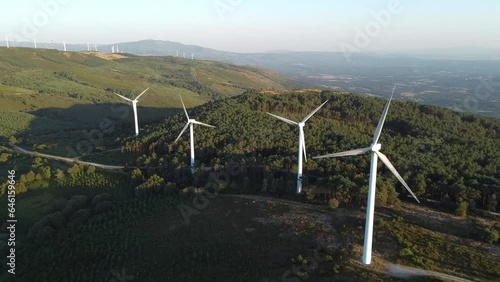 aerial view of eolic generators spining on the top of a hill at sunset