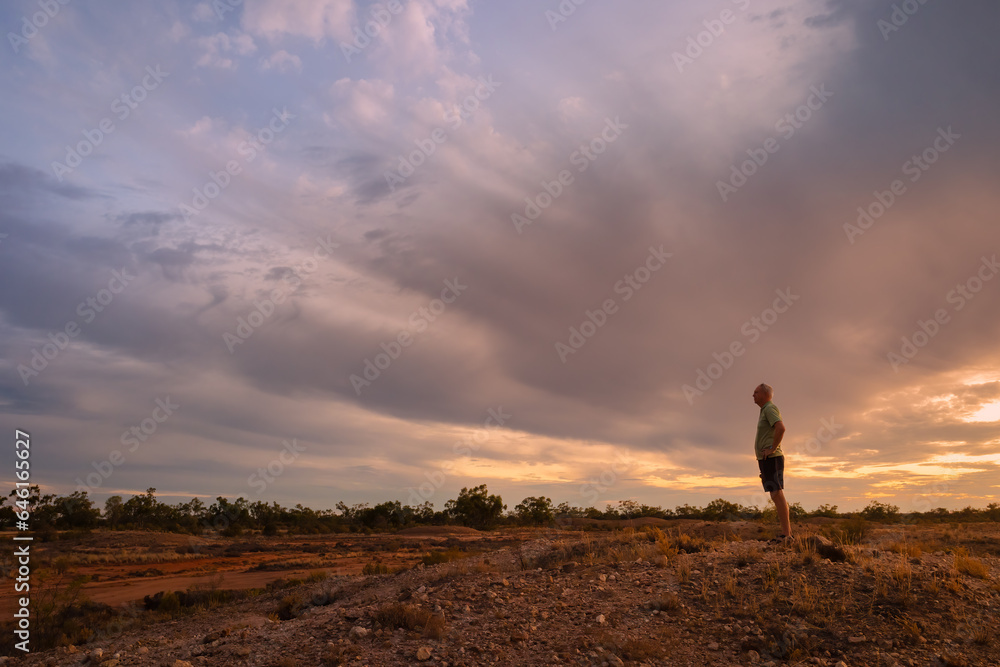 A man standing on a rise in the semi arid country of Australia at sunset in Currawinya National Park.
