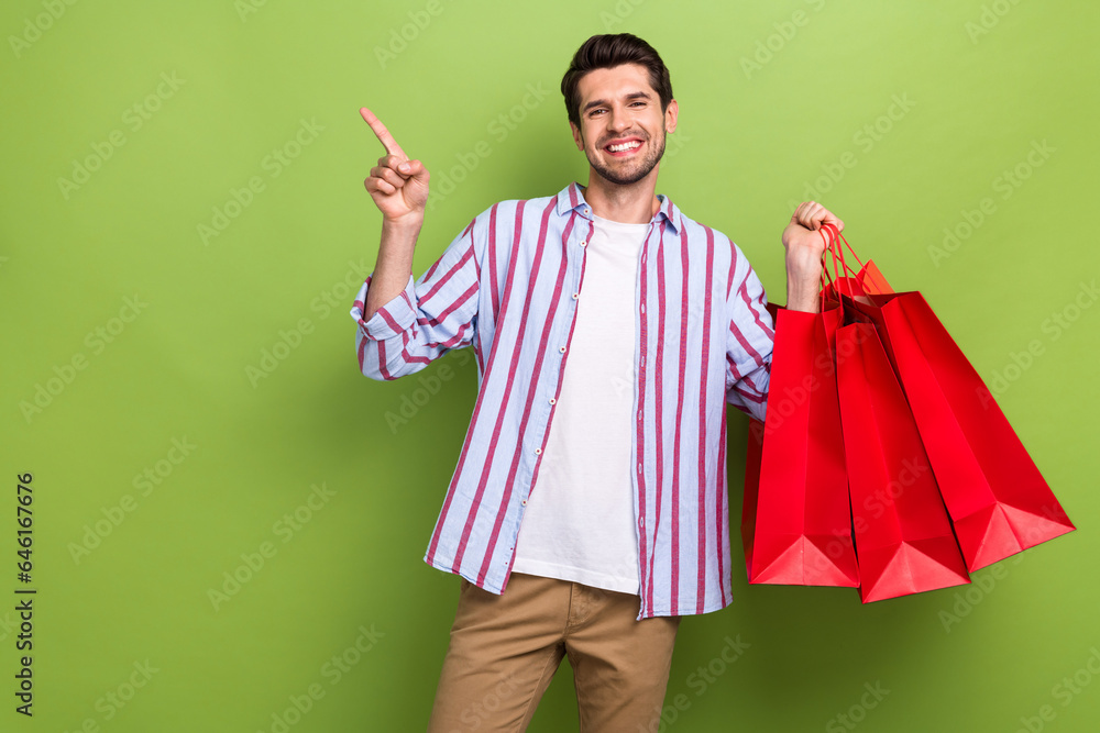 Photo of young shopaholic fashion addiction brand direct finger empty space hold red bargains clothes isolated on green color background Photo of young shopaholic fashion addiction brand direct finger empty space hold red bargains clothes isolated on green color background