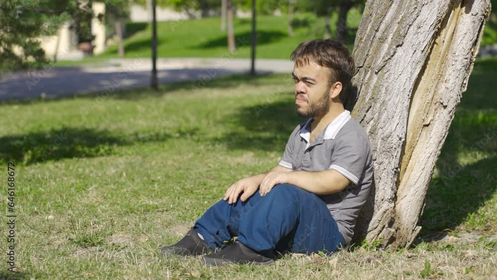 Desperate dwarf young man sits on the ground outdoors. Desperate dwarf young man sits on the ground outdoors.