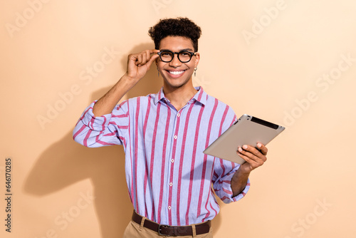 Photo of attractive young man hold tablet touch specs wear trendy striped formalwear clothes isolated on beige color background