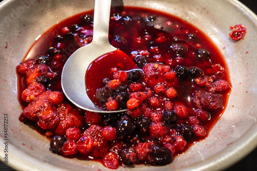 фотографія A mixed red, summer fruit compote in a bowl with a serving spoon, part of a self service breakfast buffet at a hotel