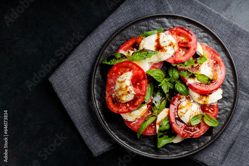 Plate of healthy classic caprese salad with ripe tomatoes and mozzarella cheese with fresh basil leaves on dark background. Close up