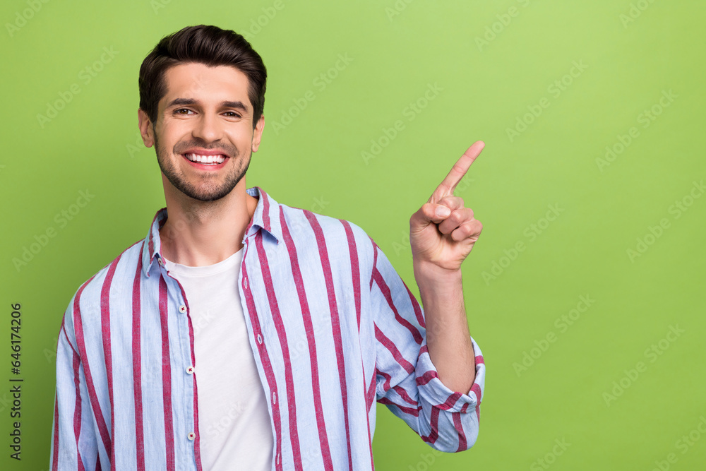 Portrait of toothy beaming man with brunet hair wear stylish clothes indicating at sale empty space isolated on green color background Portrait of toothy beaming man with brunet hair wear stylish clothes indicating at sale empty space isolated on green color background