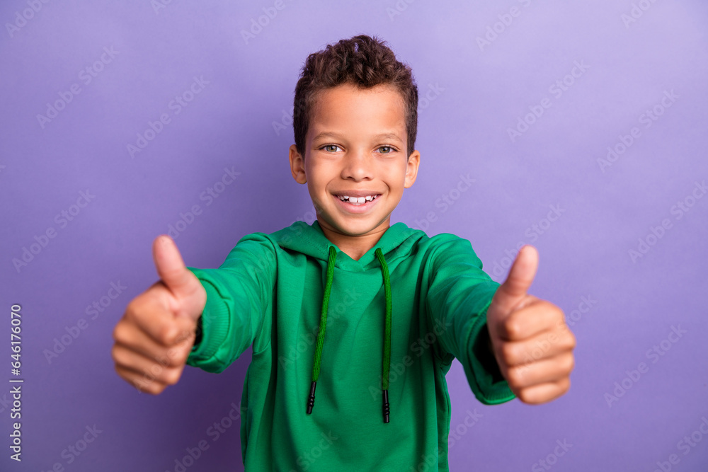 Photo of confident pretty small boy wear green sweatshirt showing you two thumbs up isolated violet color background Photo of confident pretty small boy wear green sweatshirt showing you two thumbs up isolated violet color background