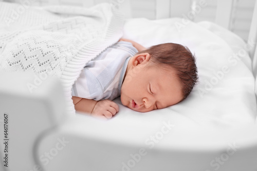 Cute newborn baby sleeping under plaid in crib