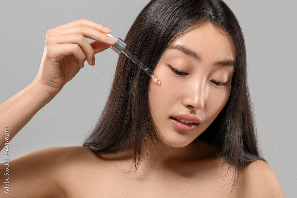 Beautiful young woman applying cosmetic serum onto her face on grey background Beautiful young woman applying cosmetic serum onto her face on grey background