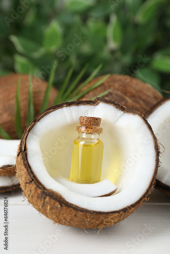 Bottle of organic coconut cooking oil, leaf and fresh fruits on white table, closeup