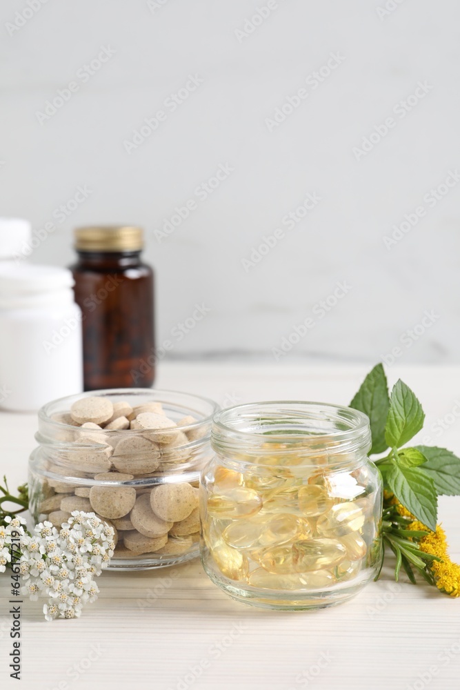 Jars with different pills, flowers and herbs on white wooden table, space for text. Dietary supplements Jars with different pills, flowers and herbs on white wooden table, space for text. Dietary supplements