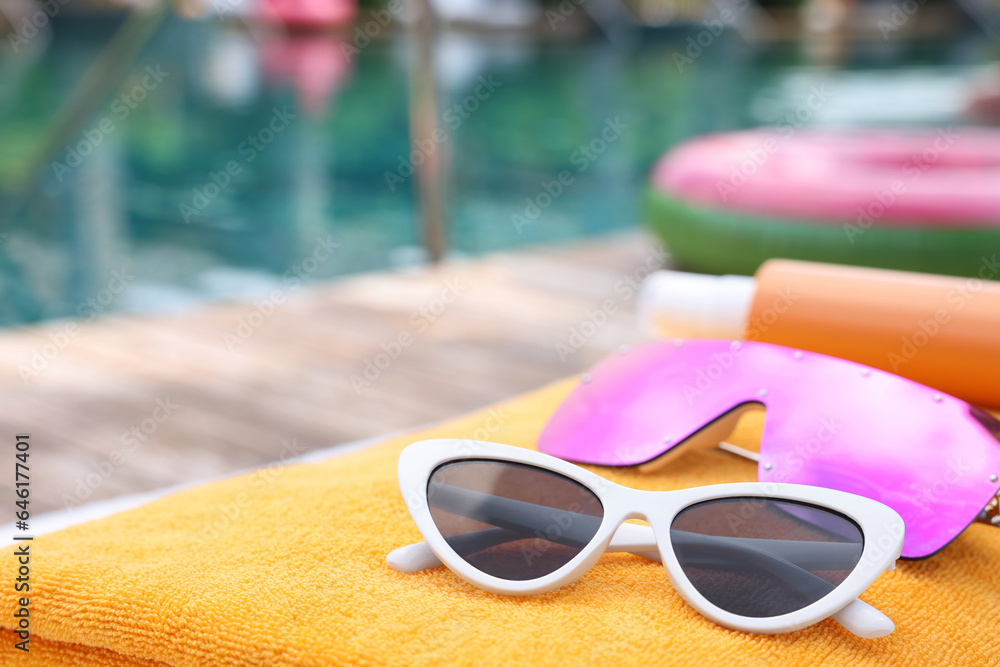 Beach towel and sunglasses near outdoor swimming pool at luxury resort, closeup. Space for text