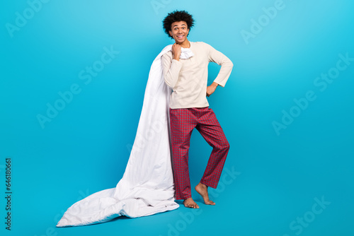 Full body photo of attractive young man holding soft blanket posing dressed white pajama clothes isolated on blue color background