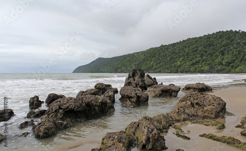 Etty Bay beach with rocks, sand, the ocean and trees on a cloudy day in Far North Queensland, Australia