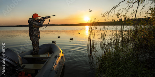 waterfowl hunter shooting into flying duck during duck hunting at sunrise or sunset. bunner with copy space.
