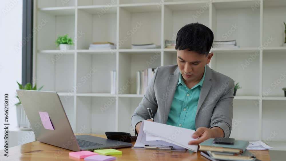 Young Asian businessman working on a desk calculating financial reports in the office. Finance, Annual taxes, Checking documents, economic concepts, accounting, economics Young Asian businessman working on a desk calculating financial reports in the office. Finance, Annual taxes, Checking documents, economic concepts, accounting, economics