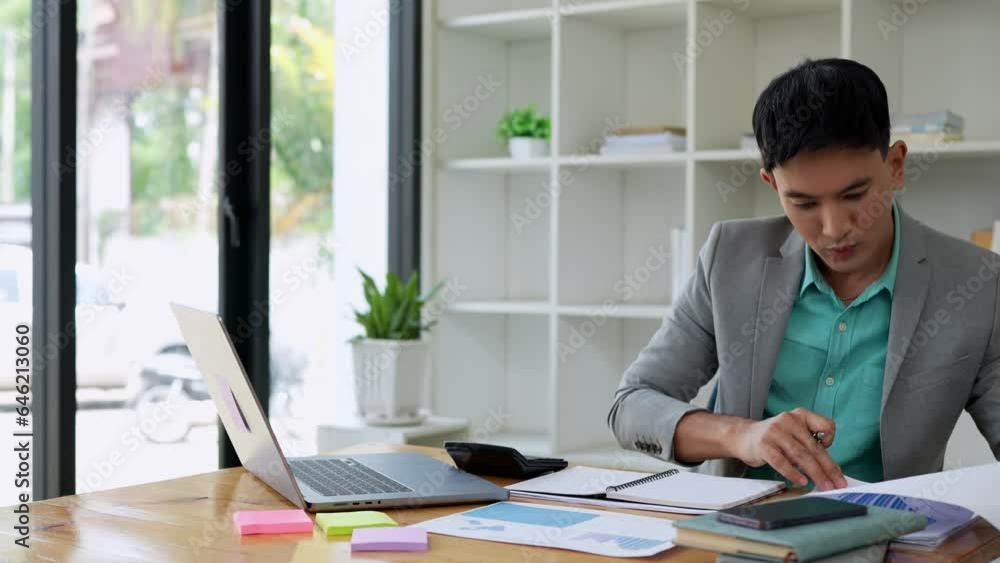 Young Asian businessman working on a desk calculating financial reports in the office. Finance, Annual taxes, Checking documents, economic concepts, accounting, economics Young Asian businessman working on a desk calculating financial reports in the office. Finance, Annual taxes, Checking documents, economic concepts, accounting, economics