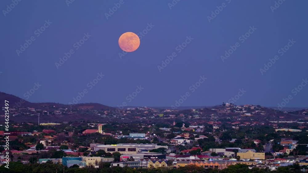 Large full blue supermoon glows red, pan right to left above willemstad curacao
