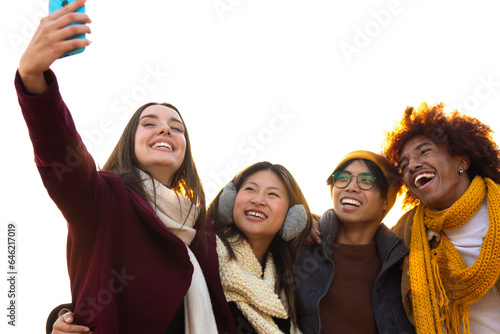 Happy multiracial college student friends taking selfie together in a sunny winter day using mobile phone. Copy space.