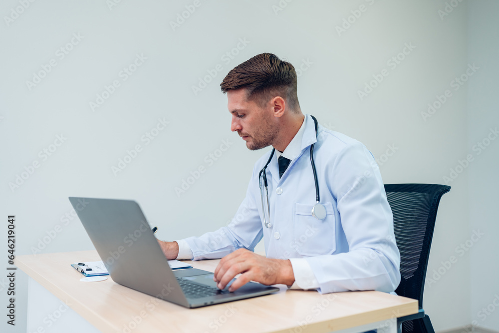 Male Doctor expert wearing white coat using laptop and reading clipboard report at work in hospital. Male Doctor expert wearing white coat using laptop and reading clipboard report at work in hospital.