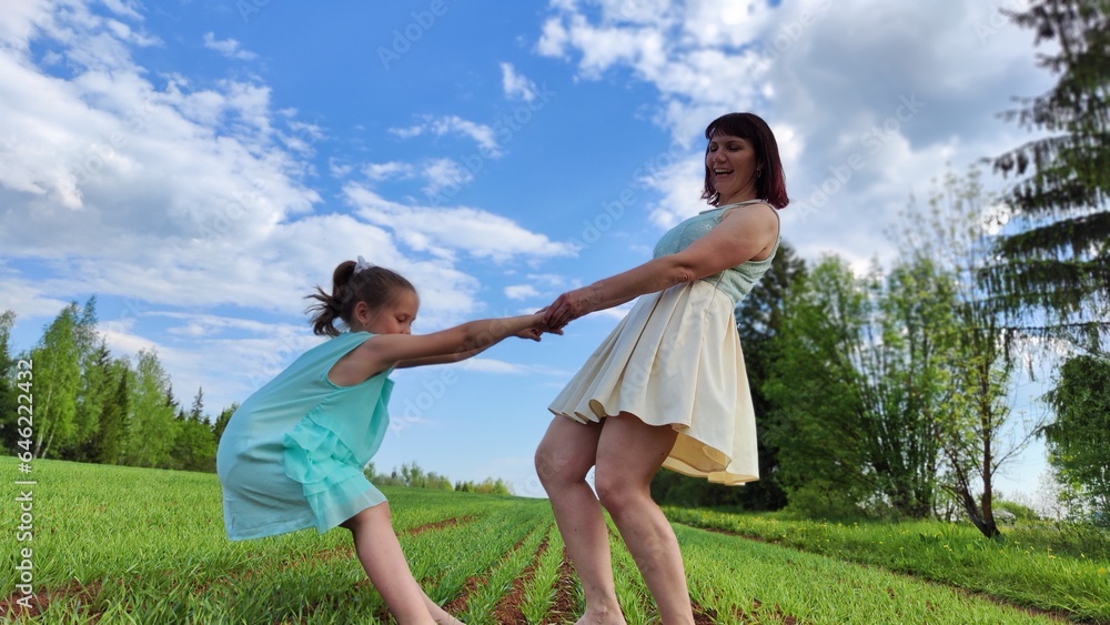 Happy mother and daughter enjoying rest, playing and fun on nature in green field. Woman and girl resting outdoors in summer and spring day