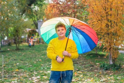 Cute boy dressed in yellow long sleeve standing under a colorful umbrella. A child in the autumn park posing with rainbow umbrella.