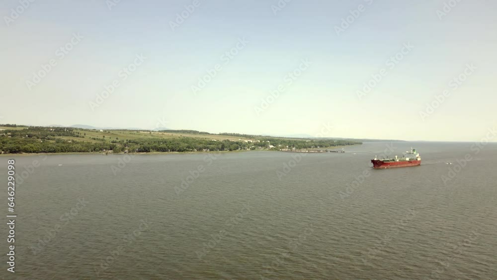 As you glide above the river, you'll be drawn towards a magnificent red cargo ship cruising gracefully, a testament to the bustling maritime activity of the region. As you glide above the river, you'll be drawn towards a magnificent red cargo ship cruising gracefully, a testament to the bustling maritime activity of the region.