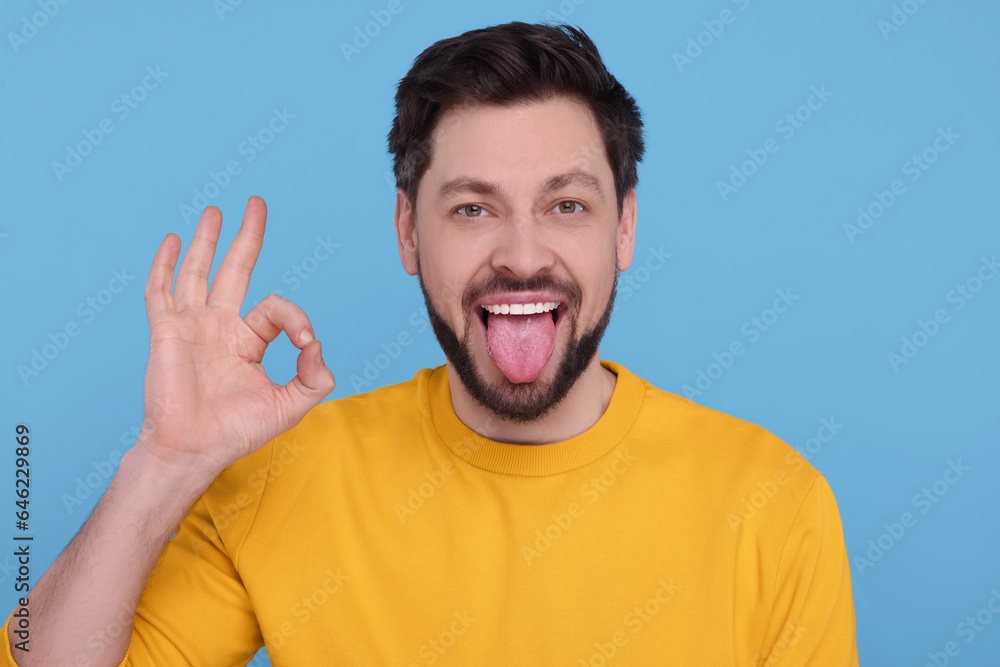 Happy man showing his tongue and making ok gesture on light blue background Happy man showing his tongue and making ok gesture on light blue background