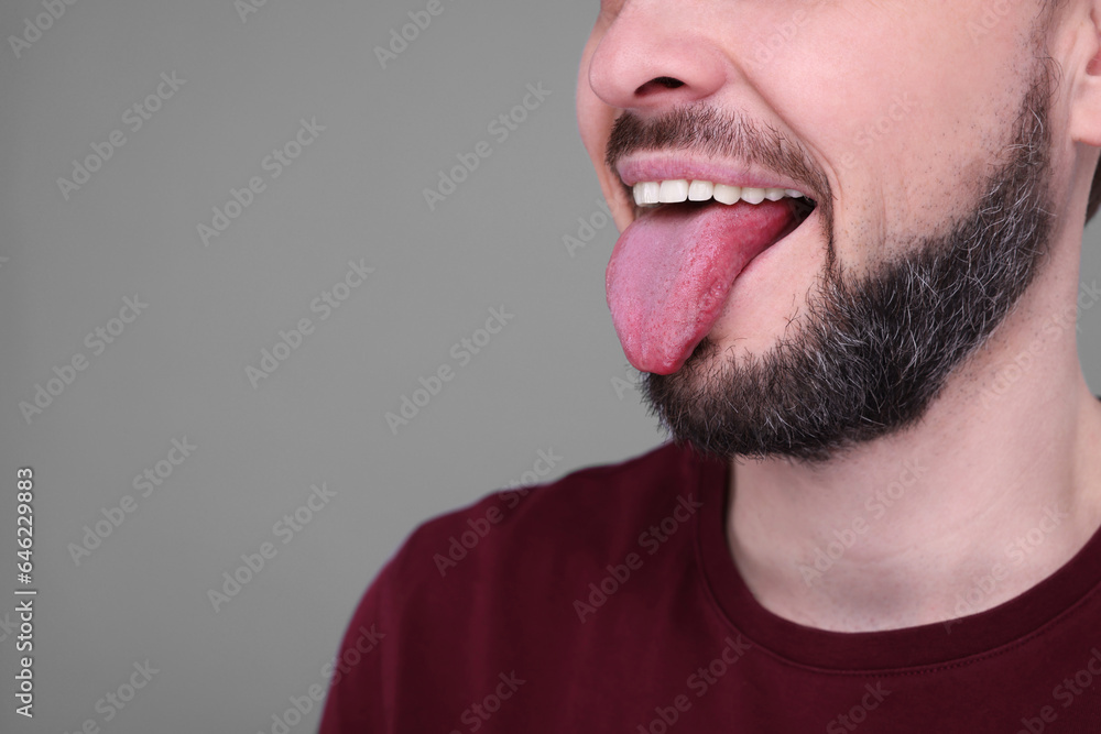 Fototapeta premium Happy man showing his tongue on light grey background, closeup. Space for text