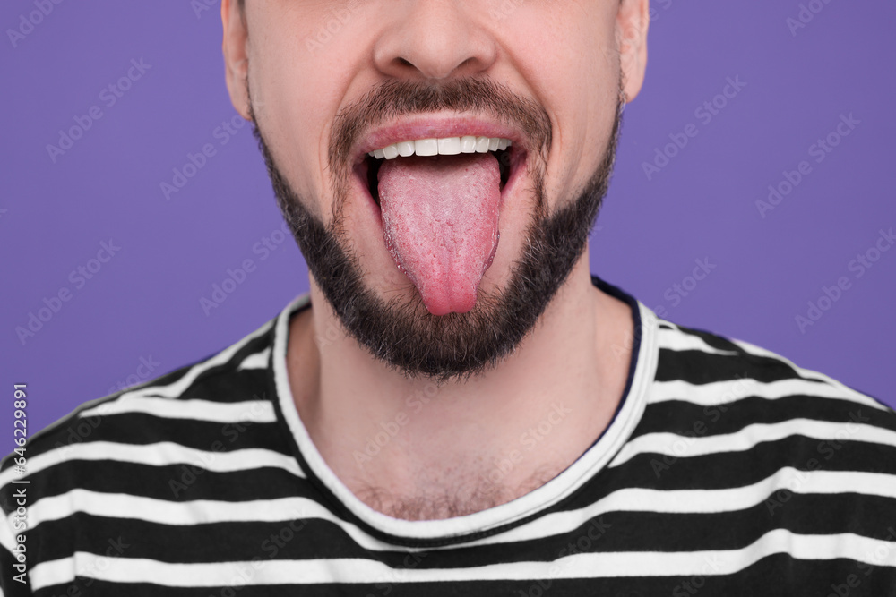 Obraz premium Happy man showing his tongue on purple background, closeup