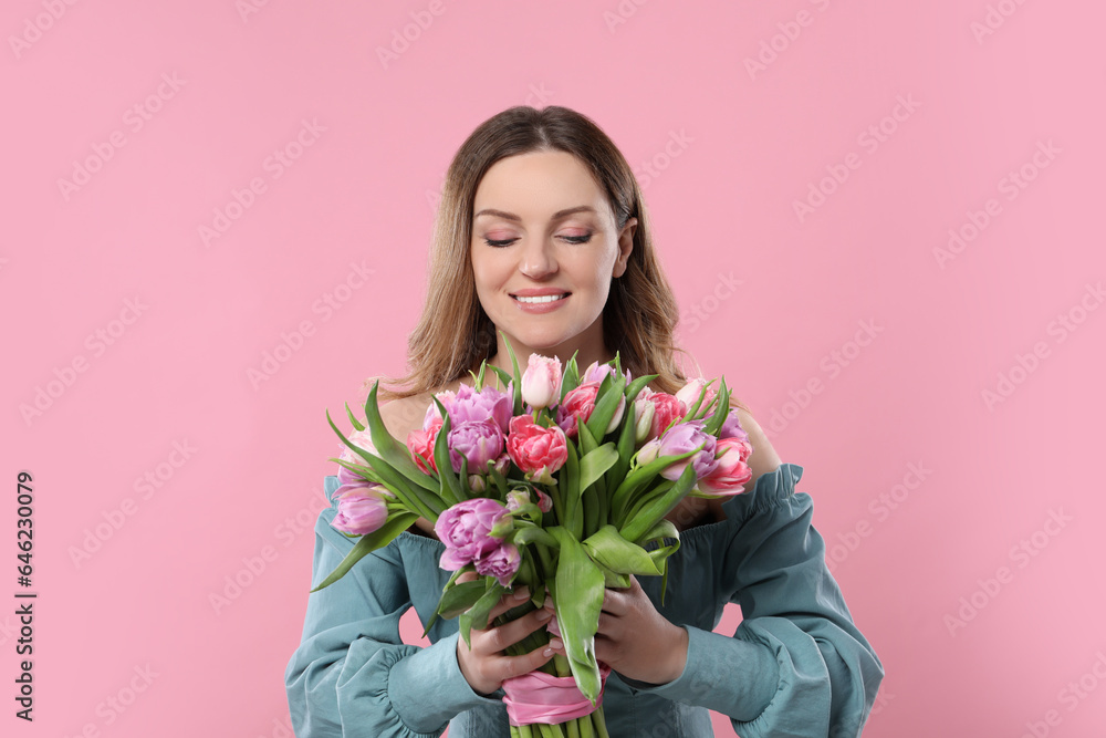 Happy young woman with bouquet of beautiful tulips on pink background